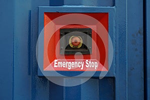 Red Emergency stop button placed on the wall of blue container of electric power pack.