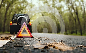 Red emergency stop sign red triangle warning sign and broken black SUV car  on country road in summer rain