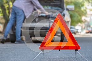 Red emergency stop triangle sign afore Destroyed car in car crash traffic accident on city road. Man driver looking on Smashed