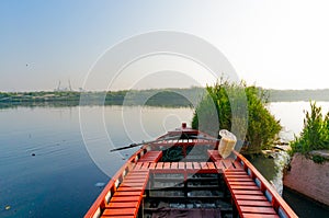 Red empty boat moored near some bushes on a blue serene river