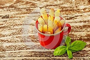Red enameled cup with potato fries decorated with two cherry tomatoes, over wooden table. Top view.