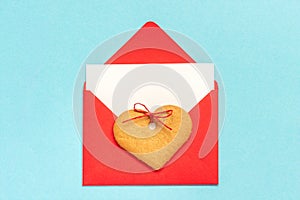 Red envelope with blank white card for text and heart shaped ginger cookies on blue background