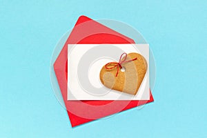 Red envelope with blank white card for text and heart shaped ginger cookies on blue background