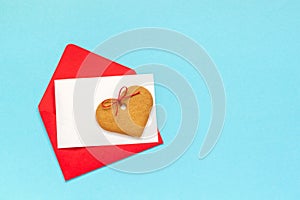 Red envelope with blank white card for text and heart shaped ginger cookies on blue background