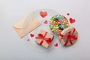 Red envelope with candy and gift box and Valentines hearts on colored background. Flat lay, top view. Romantic love