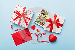 Red envelope with candy and gift box and Valentines hearts on colored background. Flat lay, top view. Romantic love