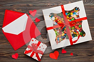 Red envelope with candy and gift box and Valentines hearts on colored background. Flat lay, top view. Romantic love