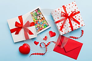 Red envelope with candy and gift box and Valentines hearts on colored background. Flat lay, top view. Romantic love