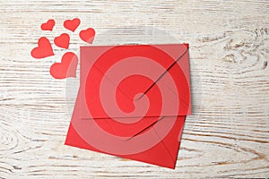 Red envelopes and paper hearts on white wooden table, flat lay. Love letters