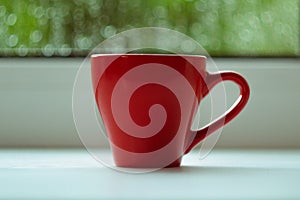 The red espresso cup on white windowsill. On background window and rain.