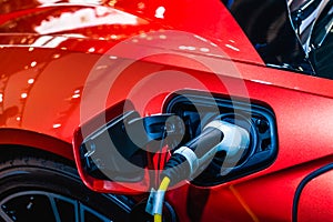 Red EV Car at charging station with the power cable supply plugged in. Power supply connect to electric vehicle for charging the