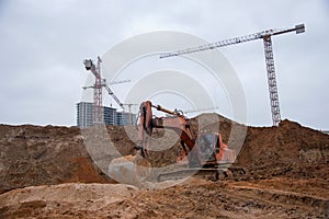 Red excavator digg trench for laying sewer pipes and main reticulation systems. Backhoe during earthworks on construction site.