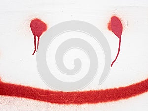 Red face on the white wall. Eyes and lips drawn on the concrete surface, red paint flowed on the eyes