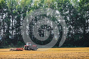 Red farming tractor is working in the field. Disc harrow for crushing stubbles.