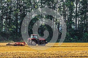 Red farming tractor is working in the field. Disc harrow for crushing stubbles.