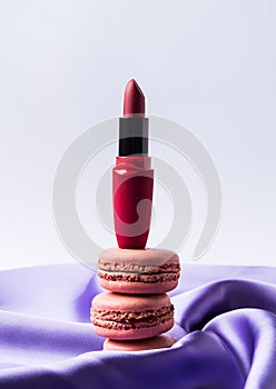 Red fashion lipstick and pink macaroons on purple silk fabric and gray background