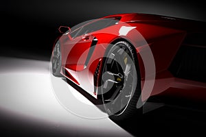 Red fast sports car in spotlight, black background. Shiny, new, luxurious.