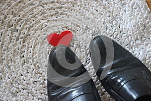 Red felt heart under men`s black shoes on crochet carpet background - symbolizes relationship of unrequited love