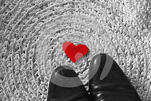 Red felt heart under men`s black shoes on crochet carpet background - symbolizes relationship of unrequited love