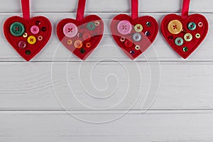 Red felt hearts crafts decorated with beads and buttons on white background.