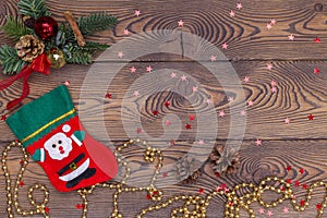 Red felt stocking with the image of Santa, fir branches, cones and Christmas decorations, snowflakes, beads on a wooden table. Top