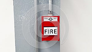 Red fire alarm button for pull out in emergency case happen in stalled on gray or grey steel pole with white wall background