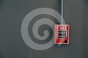A red fire alarm pull station on the grey wall.