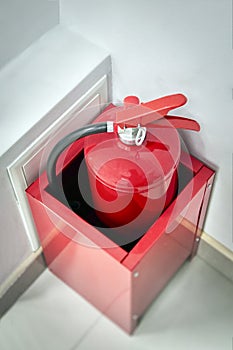 Red fire extinguisher in box against the white wall.