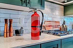 Red fire extinguisher beside cooktop on the countertop inside kitchen of home