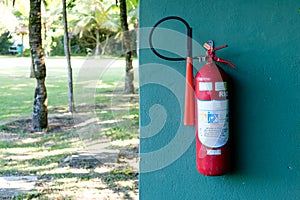 Red fire extinguisher on green wall, with garden on the background