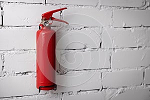 Red fire extinguisher hanging on white brick wall. copy space