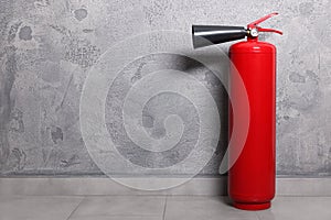 Red fire extinguisher near grey wall, space for text