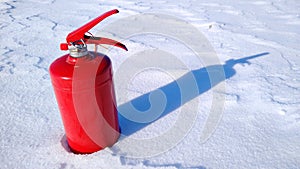 Red fire extinguisher on a winter surface of white shiny snow with a shadow from snow drifts