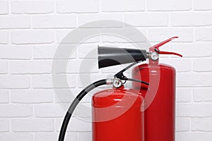 Red fire extinguishers near white brick wall, space for text