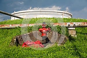 A red fire monitor in front of a crude oil storage tank
