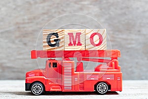 Red fire truck hold block in word GMO abbreviation of Genetically Modified Organisms on wood background