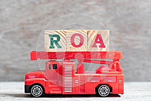 Red fire truck hold block in word ROA Abbbreviation of Return on assets on wood background