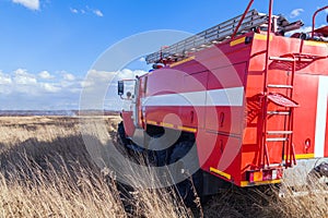 Red firetruck car Ural rides through the autumn field with yellow and faded grass against the blue sky and clouds. The concept