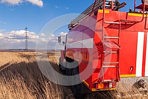 Red firetruck car Ural rides through the autumn field with yellow and faded grass against the blue sky and clouds. The concept