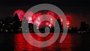 Red Fireworks light up the night sky over a city skyline with river reflections