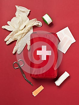 Red first aid medical kit bag with scissors, tape and gloves top view flat lay from above over red