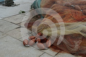 Red fishing net with red-brown floats piled on the pavement in port ready for loading on fishing boat.