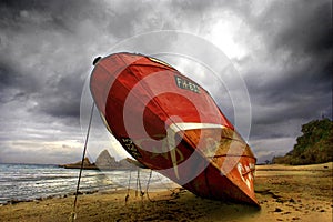Red fishing vessel beached on a beach.