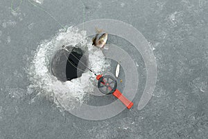 Red fishingrod next to a hole in the ice and a jumping perch