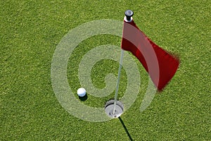 Red flag on green with golf ball.