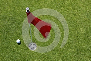 Red flag on green with golf ball.