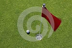 Red flag on green with golf ball.