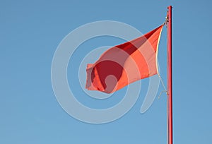 Red flag waving to indicate danger with the background of blue s