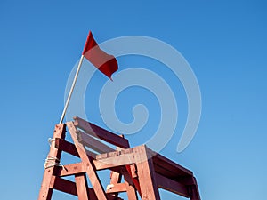 Red flag on a wooden platform. Flag as a symbol of danger. Bathing is prohibited. Beach on the sea. The concept of rescue work