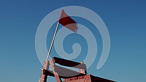 Red flag on a wooden rescue tower. Symbol of danger. A flag prohibiting swimming on the beach.